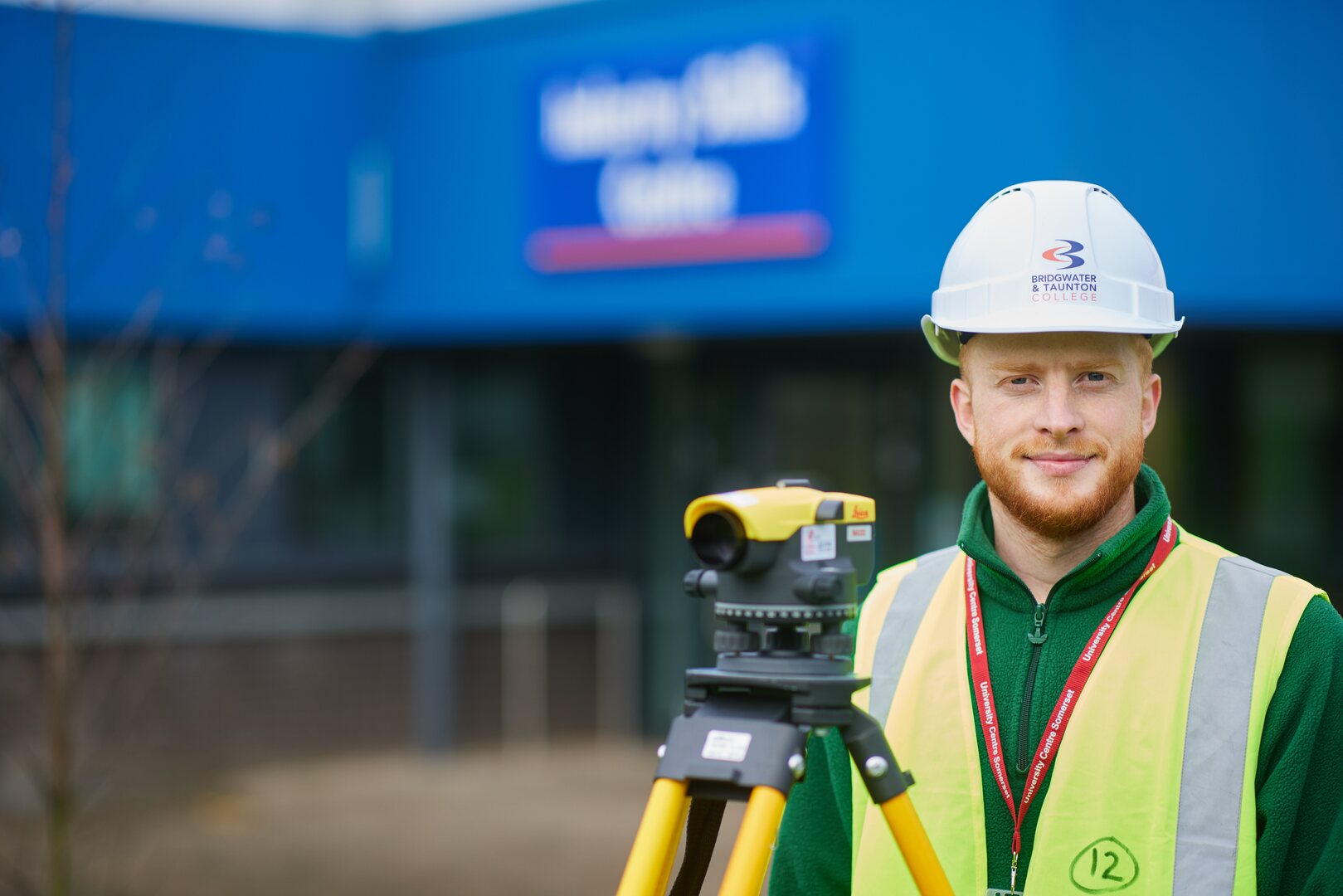 Construction student in front of Industry Skills Centre with surveying equipment